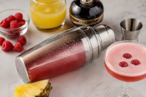 Bartender shaking a French martini cocktail with vodka, Chambord, and pineapple juice in a metal cocktail shaker