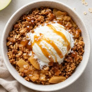 Bowl of apple crisp with vanilla ice cream and caramel drizzle