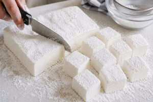 Cutting a homemade marshmallow batch into fluffy squares dusted with powdered sugar and cornstarch