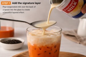 Pouring evaporated milk over a spoon to create layered Thai tea