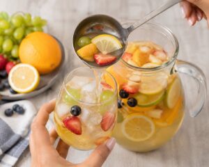 Pouring homemade white sangria from a pitcher into a glass filled with ice and fruit