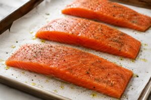 Seasoned raw steelhead trout fillets on a parchment-lined baking sheet before baking
